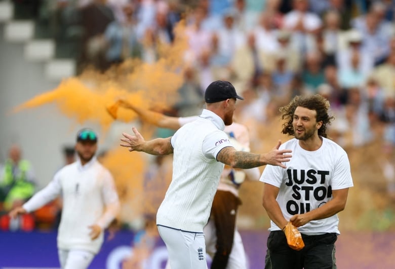 A man with his arms outstretched tries to stop a protester on a cricket pitch.