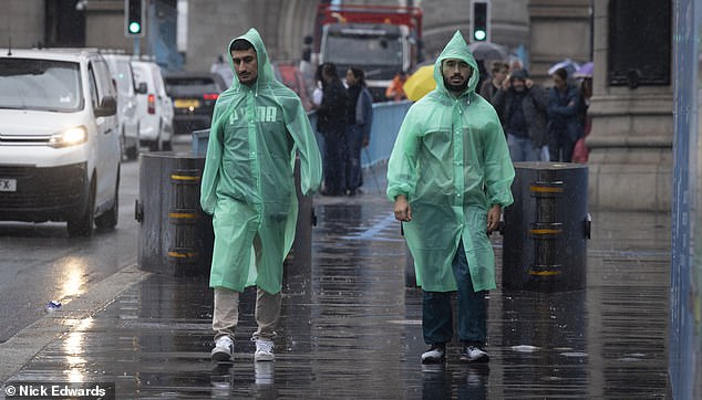 Two people dressed in green ponchos look glum in the rain around Tower Bridge yesterday