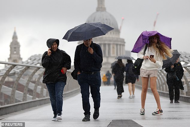 People shield themselves from the rain while crossing Millennium Bridge in London on Sunday