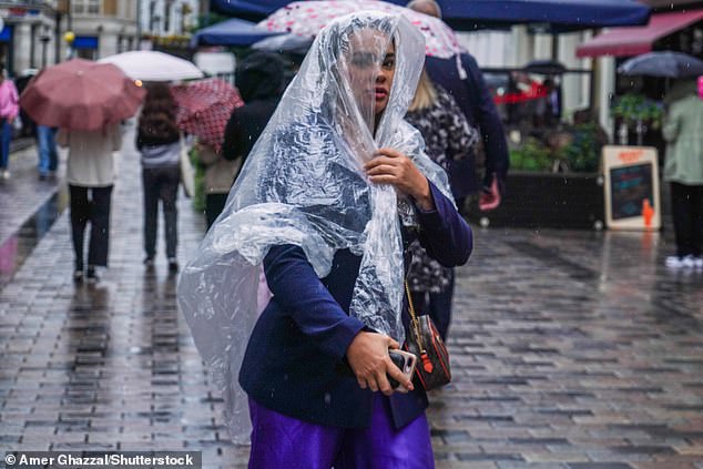 A pedestrian in London shelters under a poncho during rain showers yesterday