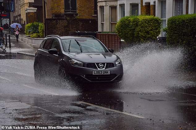 A car splashes through a large puddle in central London as a rain shower drenches the capital