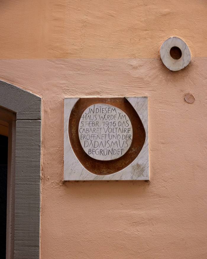 The 1966 plaque on the orange-brown wall of today’s Cabaret Voltaire by the sculptor and painter Jean Arp: a square piece of grey marble with a bronze groove and an inscription in German