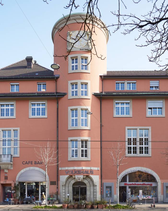 The ochre facade of Buchhandlung im Volkhaus, with two smaller buildings flanking a cylindrical building with a clock face at the top