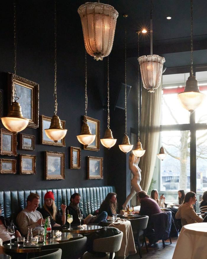 Customers in the dim interior of the Terrasse restaurant, with many oil paintings in ornate brass-coloured frames on a dark wall 