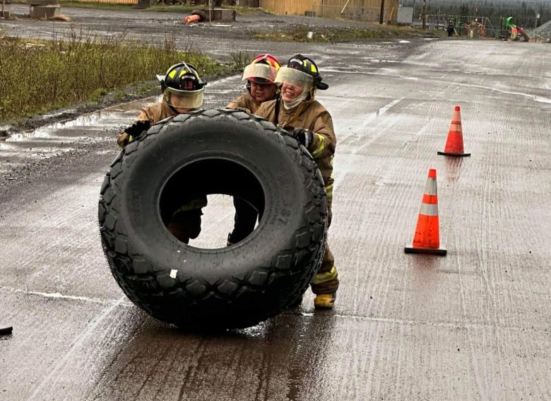 Three women flip a giant tire on a road.