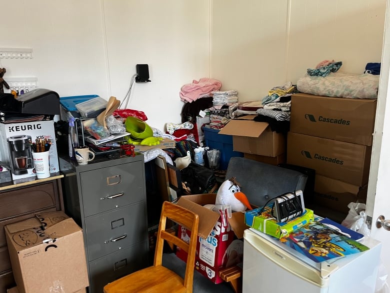 A rooom with a few tables against a wall and a chair. Donations are piled on each surface. 