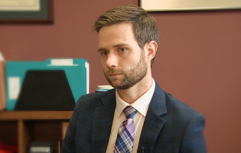 A man in his 30s in a suit. He has styled brown hair and a short brown beard.