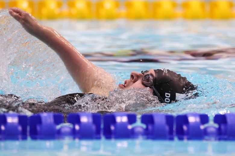 A female Par swimmer takes a breath while swimming the backstroke during an individual medley race.