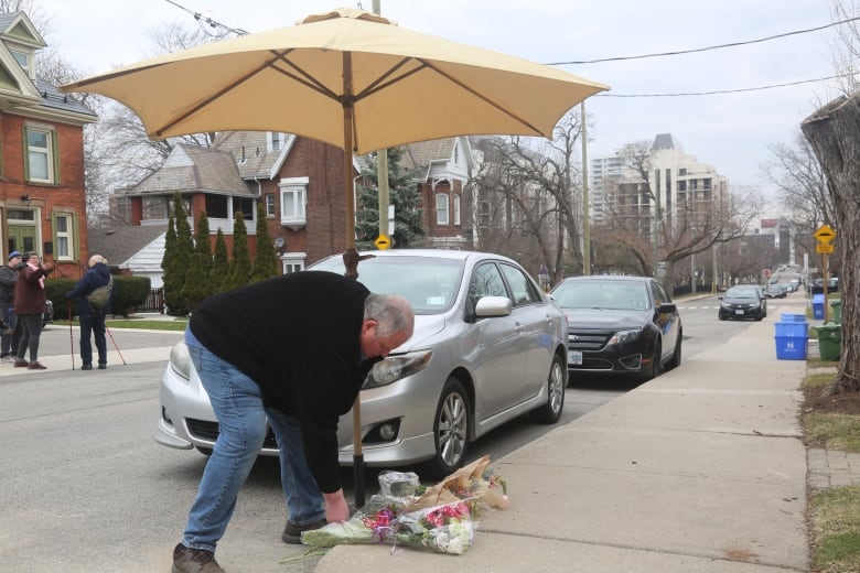 A person in jeans and a black coat organizes bouquets of flowers on the sidewalk under an umbrella