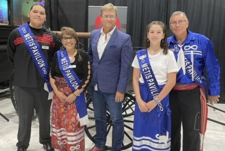 A person in a suit stands in a group of people wearing sashes that say "Métis Pavilion."