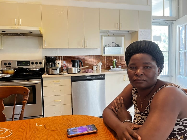 A woman with a silk black bonnet sits in a kitchen arms folded on the table. 