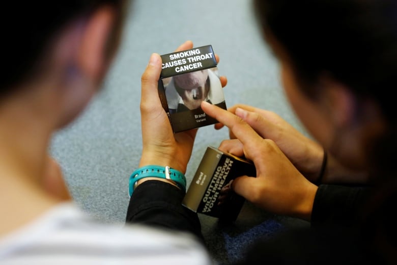 Students hold a cigarette pack that features the warning, 'SMOKING CAUSES THROAT CANCER.'