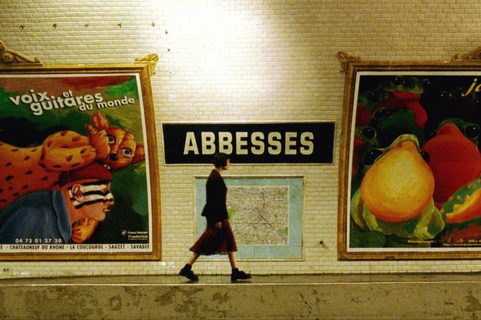 A scene from a film in which the heroine walks in front of a Paris Metro sign of Abbesses 