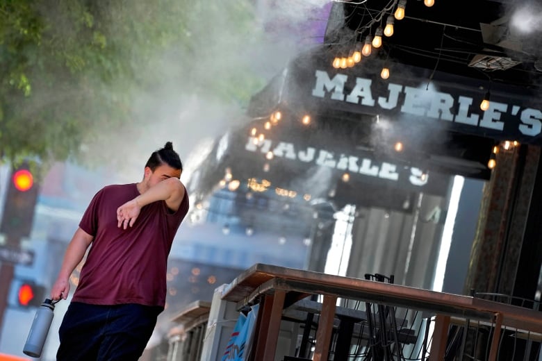 A person wipes their face with their shirt sleeve as they walk through water misters.