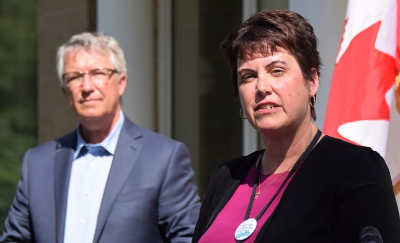 Woman speaks at podium, man seen in background