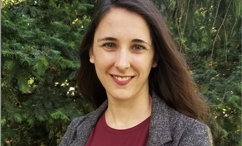 A portrait of a smiling woman with long dark hair standing in front of a tree.