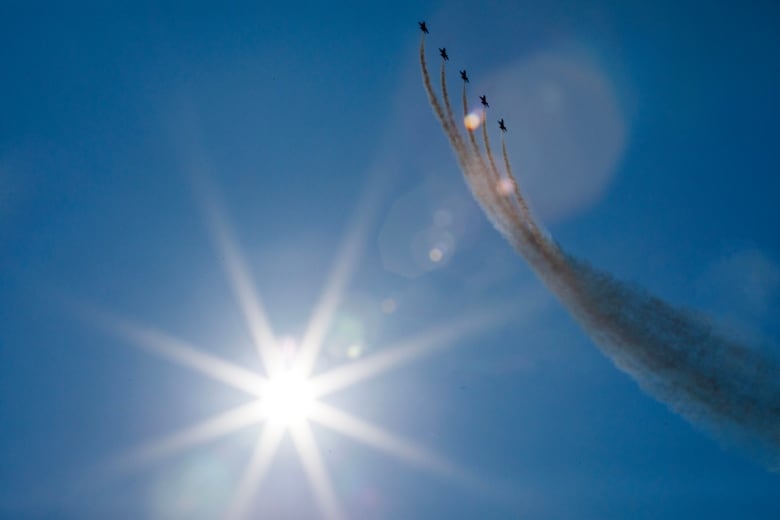 Five U.S. Navy Blue Angels practise flying over downtown Toronto ahead of an air show, the sun in view.