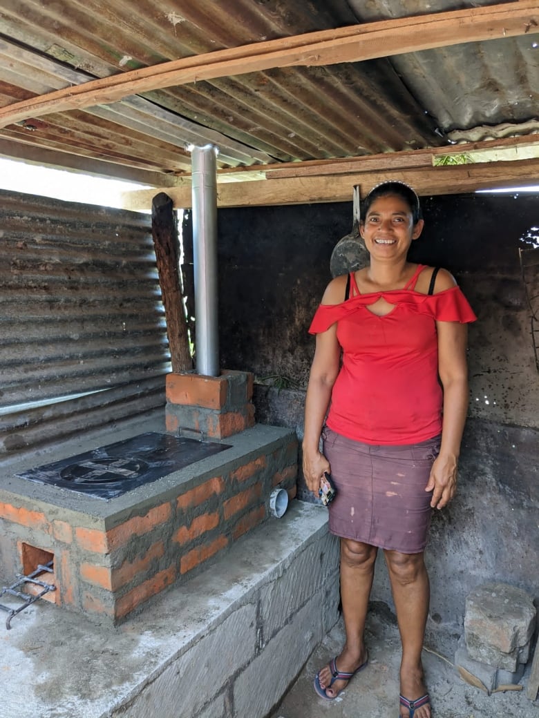 A Latinx woman stands next to a stove built by volunteers and trainees in Canada and Nicaragua respectively.