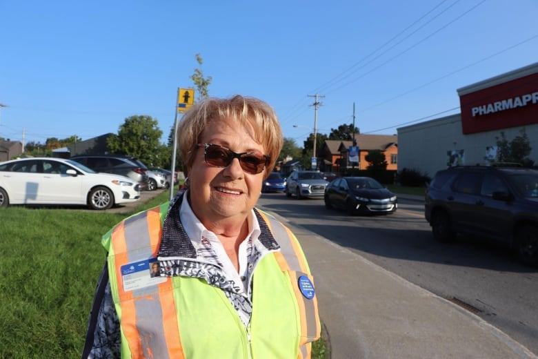 A woman looks at the camera wearing a yellow vest on the corner of a street 