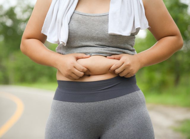 woman holding belly fat, concept of reasons you're not losing belly fat