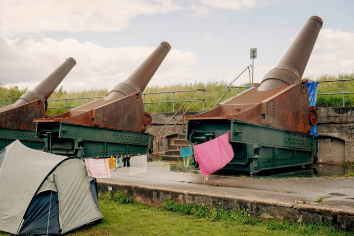 Three rusty old cannons pointing over a grass rampart at Charlottenlund Fort, with a tent behind them. Between one of the cannons and the tent, campers have strung up a washing line on which are hanging clothes and towels