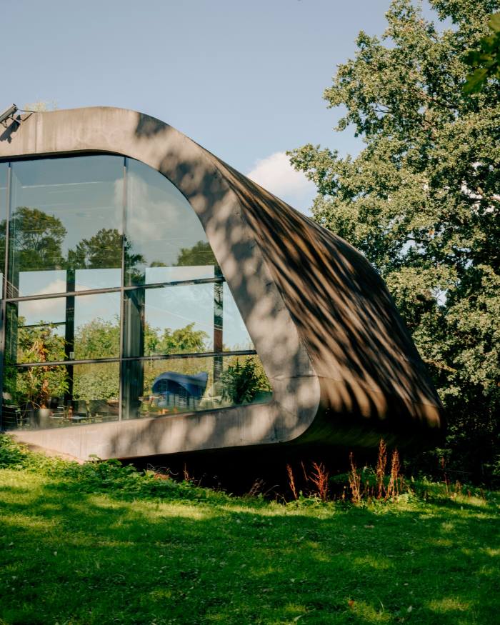 A detail of a modernist concrete and glass extension of Ordrupgaard museum, with a sloping wall curving down from the roof 