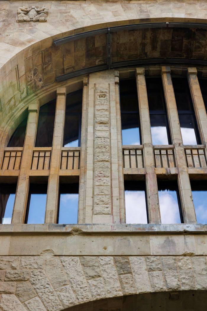 A close-up of the exterior of a building shows high windows in a stone arch