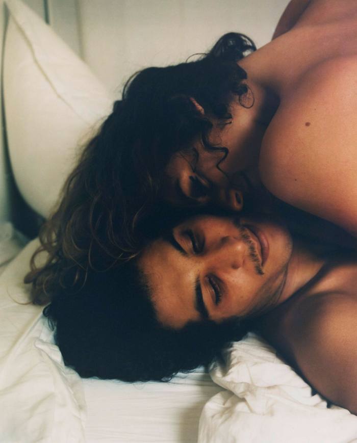 A woman and a man are seen lying on a bed from the shoulders up, seemingly naked, and embracing