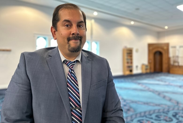 A man stands in a mosque looking at the camera. 