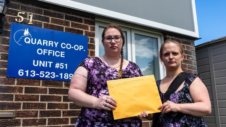 Two women in front of a building holding a yellow envelope.