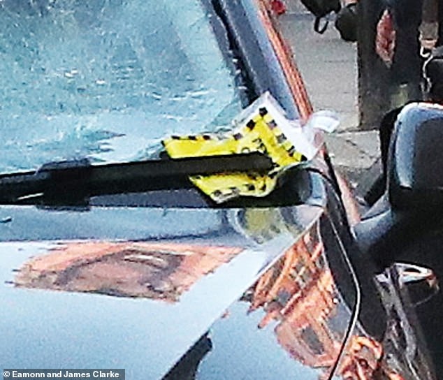 A yellow ticket can be spotted tucked behind a windscreen wiper, while a warden appears to be remonstrating with a woman nearby