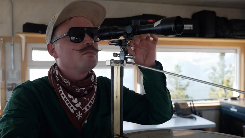 A man wearing a dark green shirt and a red and white scarf is seen in this picture as he handles a device.