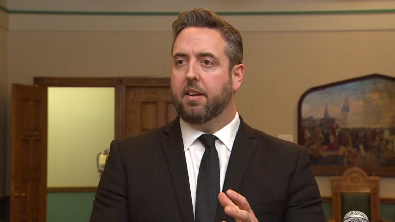 A man wearing a black suit talks to reporters.