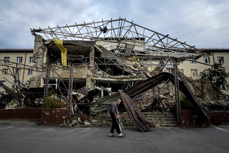 A man on crutches walks by the remnants of a destroyed building