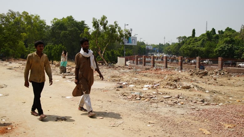 Two people walk beside some rubble left after the demolition of a shelter.