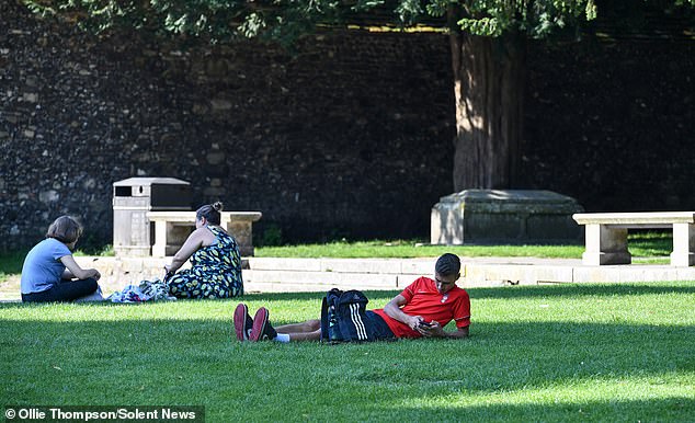 Pictured People relax in the shade of Winchester Cathedral in Hampshire this morning