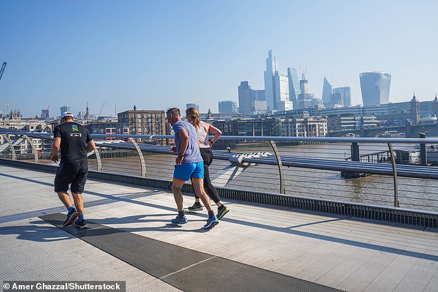 Joggers run across Millennium Bridge in London today amid the very hot weather