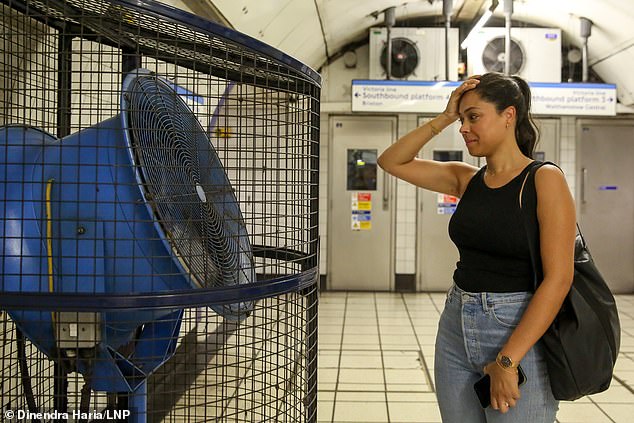 A woman cools off in front of a large fan at a London Underground station in the heat today