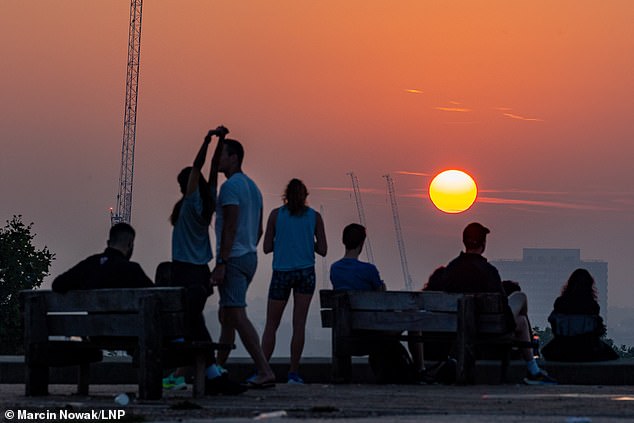 Visitors to Primrose Hill in North London enjoy a hazy sunrise today before temperatures soar