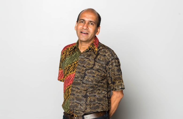 Portrait of a balding man in a patterned shirt, smiling with his hands behind his back, 