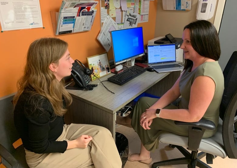 Two people sitting at a desk speak with each other.