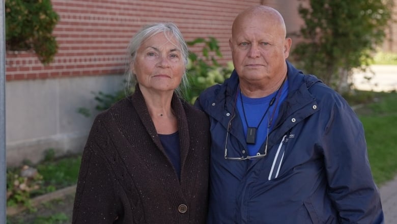 A man and a woman face stand in front of a brick building.