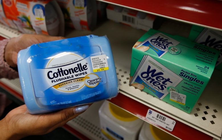 A person holds up a box labelled 'Cottonelle Flushable Wipes', next to a box marked 'Wet Ones'.