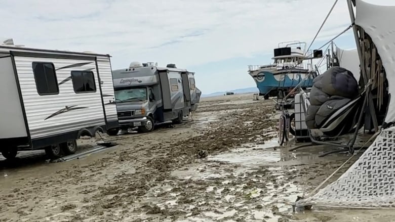 Recreational vehicle and tents are seen on a muddy site.