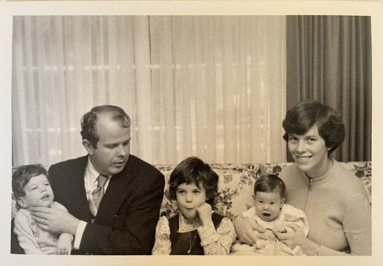 An old black and white photo shows a family on a couch, with a baby on mom's lap, a little girl in the middle and a man holding his son. 