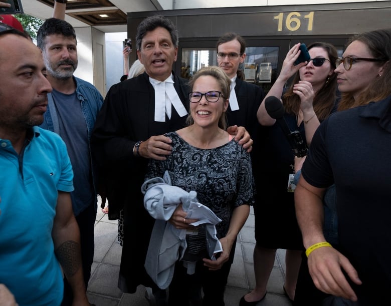 A woman smiles as her lawyer speaks behind her, surrounded by a few reporters and supporters.