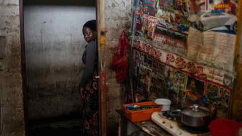 A woman stands in a doorway looking into a makeshift kitchen in a building that has been taken over