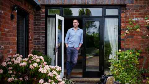 Paddy Scott, wearing jeans and a blue buttoned shirt, leans against his open french door