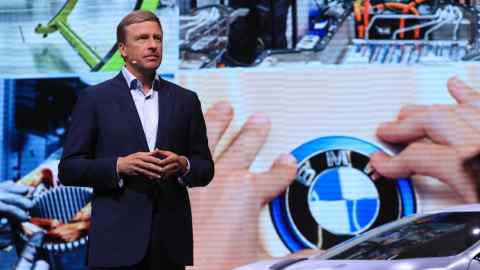 Oliver Zipse standing while wearing a headset microphone against a backdrop of BMW images