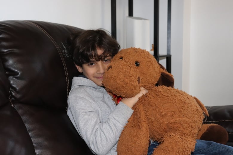 A little boy hugs a stuffed moose. 